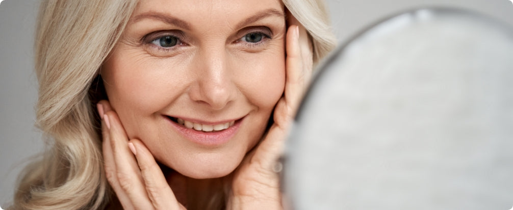 woman touching her face and smiling while looking into mirror